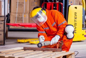 There are a lot of problems if you outsource your manufacturing. This is a photo of a man in orange coveralls using a grinding machine to cut a piece of steel.