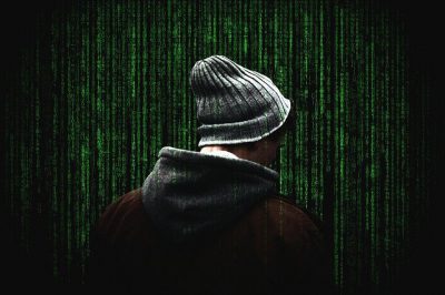 Photo of a man wearing a stocking cap with a green computer code background. I often employed white hat hackers to test our cybersecurity.