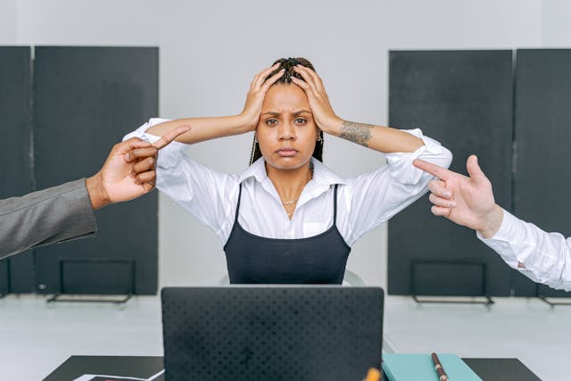 A woman at a laptop with two men's hands pointing at her, a perfect example of workplace conflict.